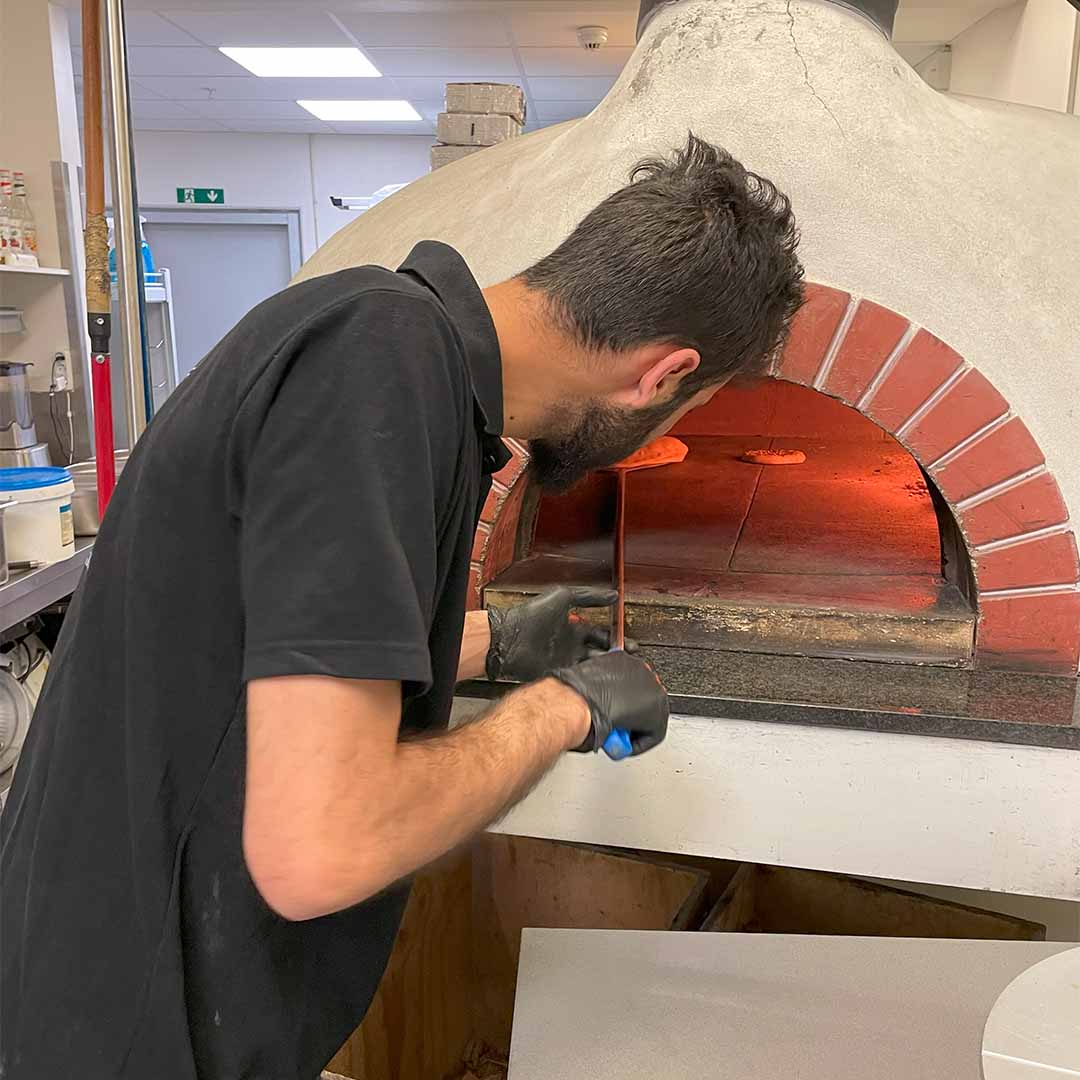 En ansat er ved at bage brød og pizzaer i en stenovnpizza hos Fire & Stone. 